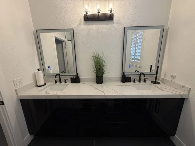 Black double vanity with a pale veined countertop, paired rectangular mirrors and black fixtures.