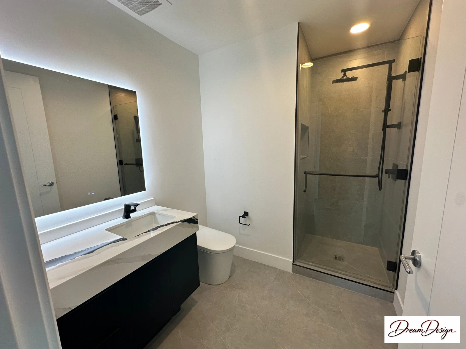 Floating dark bathroom vanity with a pale veined surface, illuminated mirror and adjacent glass shower.