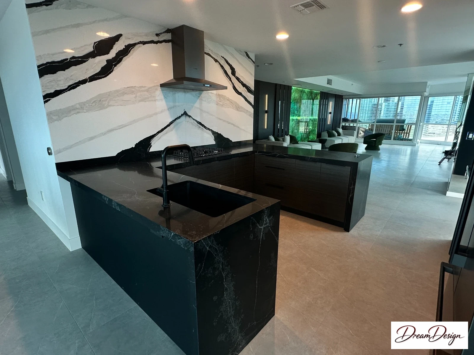 Dark kitchen cabinetry and an island beneath a striking black-and-white veined wall, with large windows beyond.