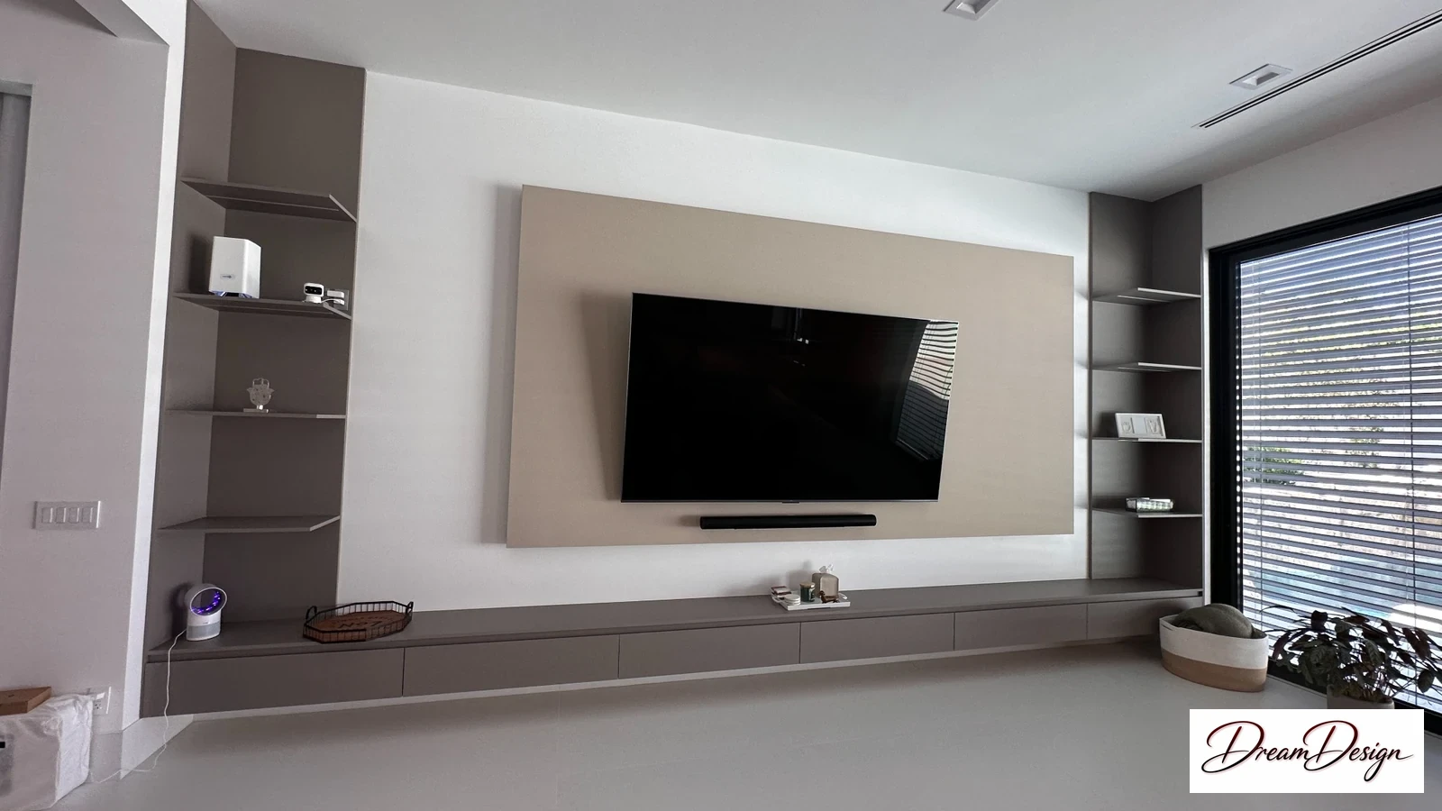 Built-in media wall with open shelving, a low cabinet and desk beside a shaded window.
