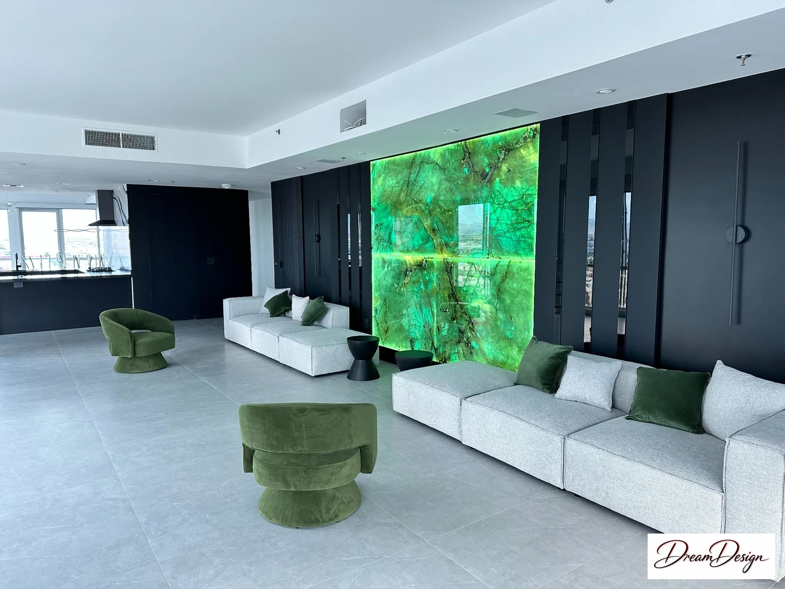 Charcoal wall cabinetry, a green illuminated feature panel, pale seating and a large tiled floor in a bright living room.