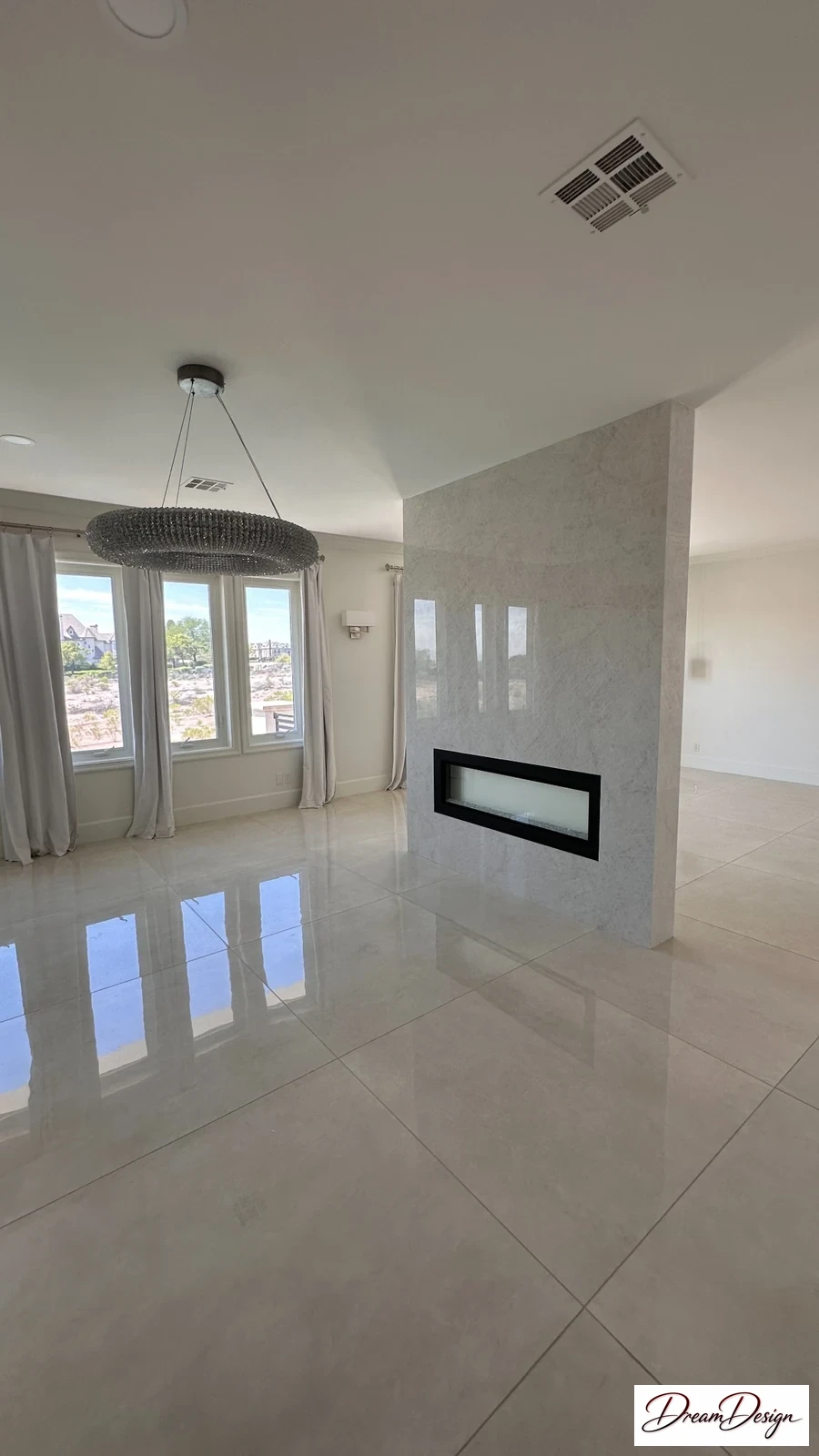 Pale large-format tile in a bright room with a long dark fireplace and glazed doors.