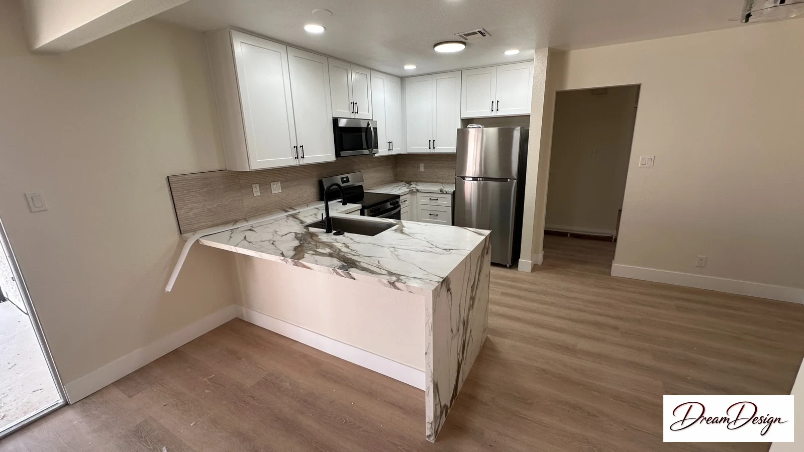 White kitchen cabinetry and a pale veined waterfall island beside a light plank floor.