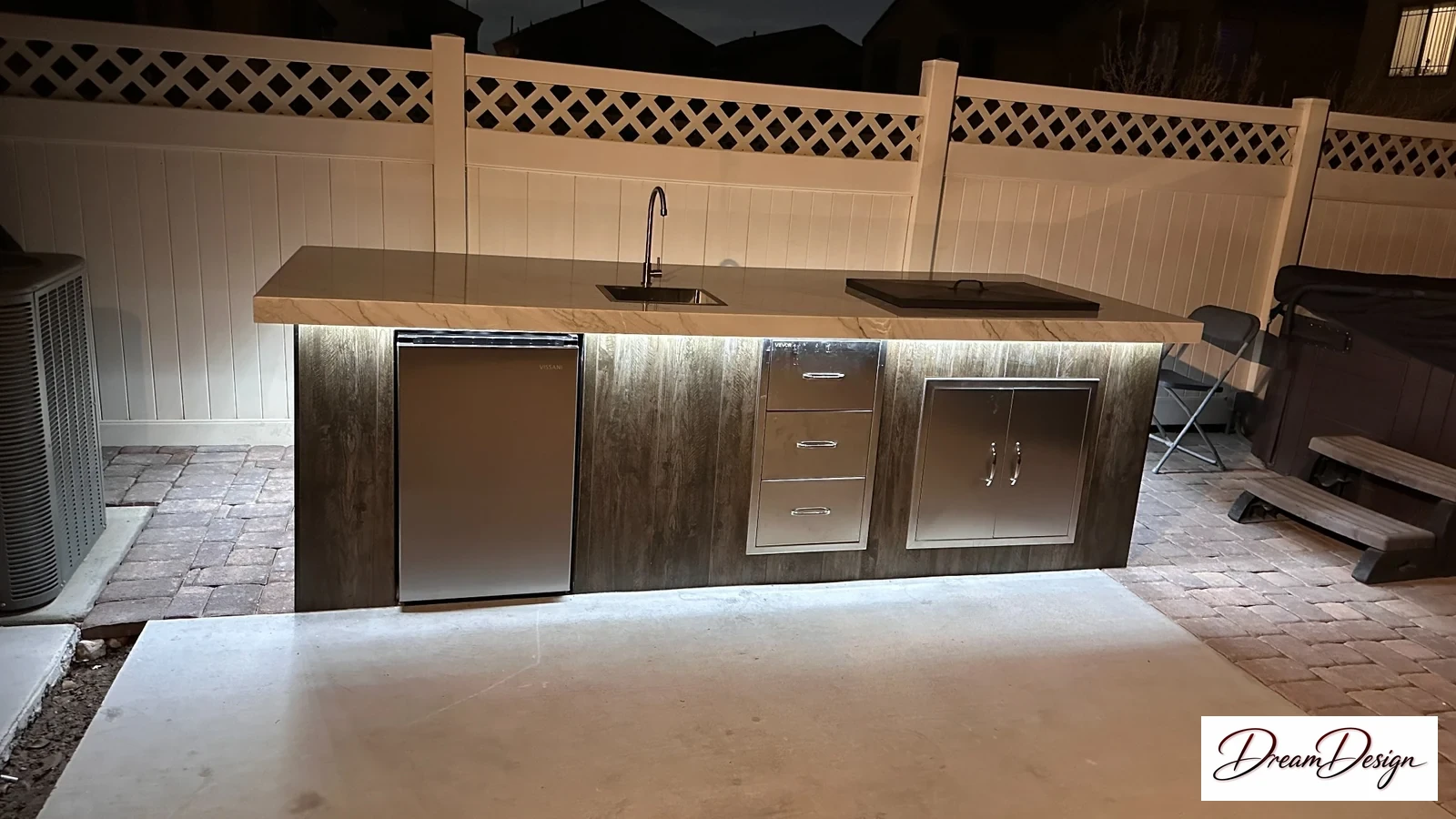 Outdoor island cabinetry with a sink, beverage refrigerator and illuminated base.