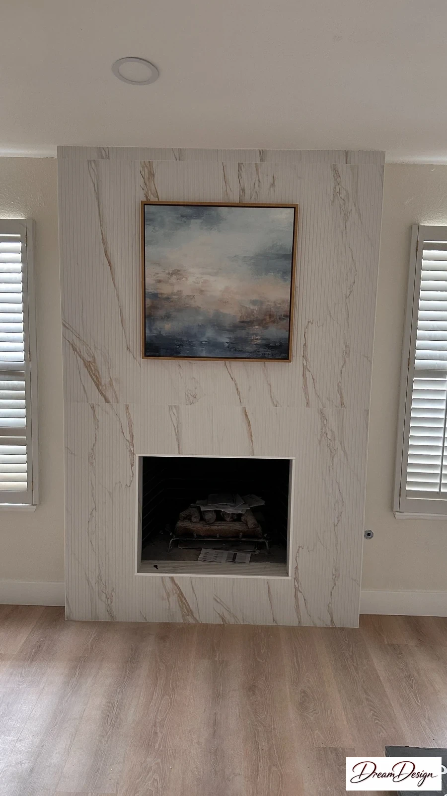 A pale full-height fireplace surround between two windows above a light plank floor.