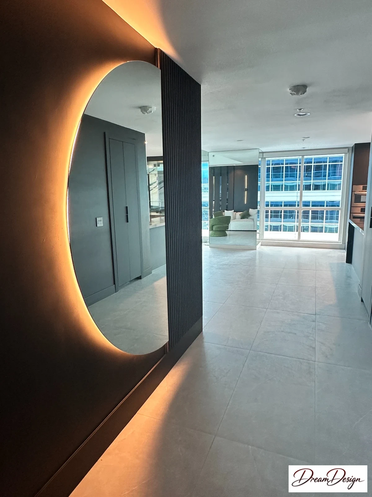 Circular backlit mirror on a dark wall beside a bright entry passage.