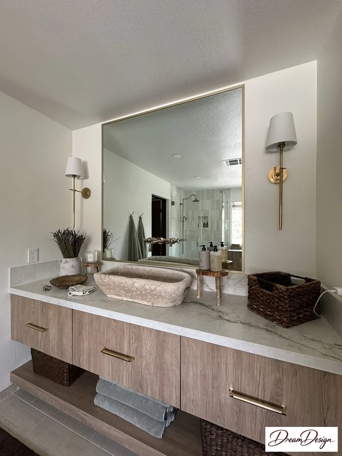 Wood-grain vanity with a sculptural vessel basin, pale veined counter, wide framed mirror and wall sconces.
