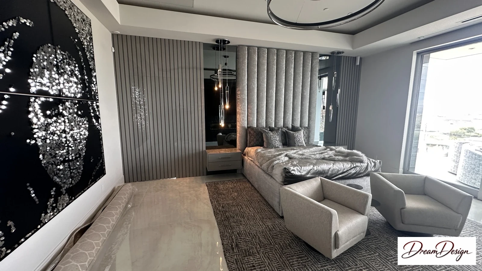 A bedroom with chairs, a bed beyond, tall ribbed wall details and a large black-and-white wall feature.