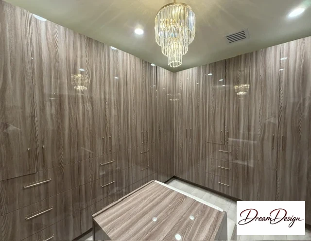 Wood-grain walk-in storage cabinetry with full-height doors, drawers and a central cabinet beneath a chandelier.