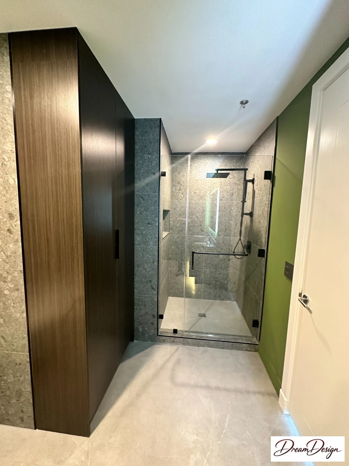 Tall wood-grain cabinetry beside a glass shower enclosure and pale tile.