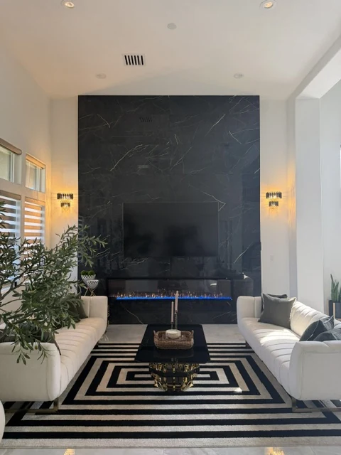 Straight-on view of a tall dark veined fireplace and television wall between light sofas.