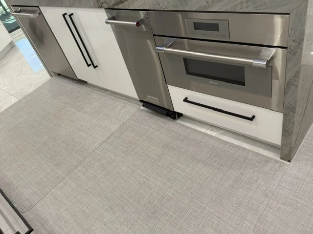 Light textured kitchen floor beside white cabinetry and stainless appliances.