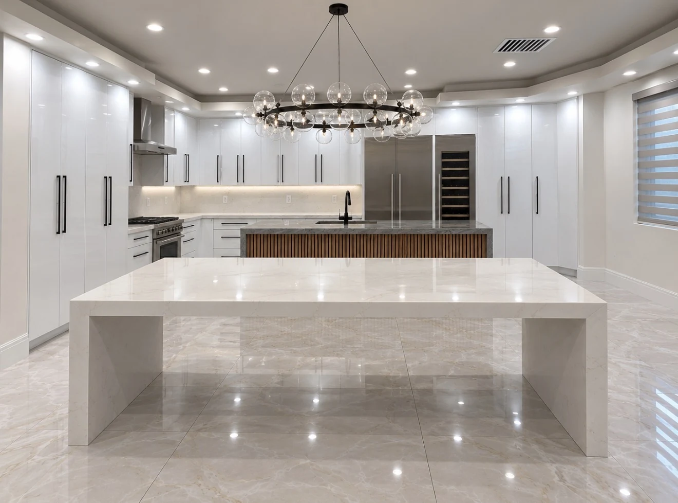 White kitchen cabinetry with black pulls, a wood-slat island front and a large pale waterfall-edge surface.