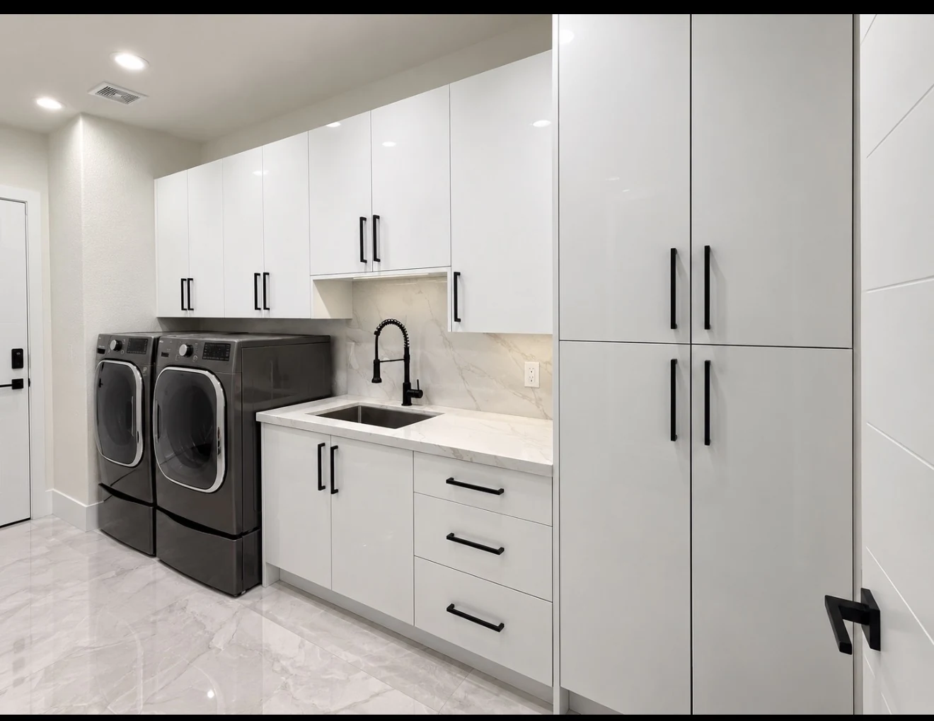White laundry cabinetry with black pulls, tall storage and a sink beside front-loading appliances.