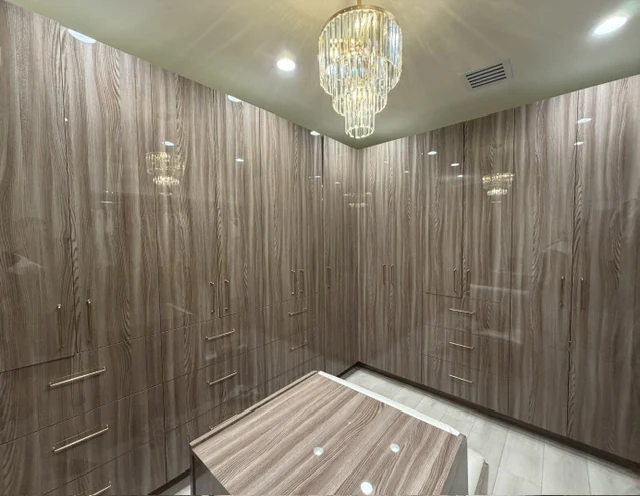 Wood-grain walk-in storage cabinetry with full-height doors, drawers and a central cabinet beneath a chandelier.
